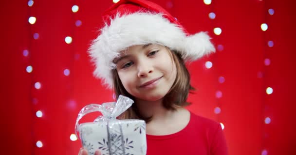 Schattig meisje in een santa hoed houdt een geschenk op een rode kerst achtergrond — Stockvideo