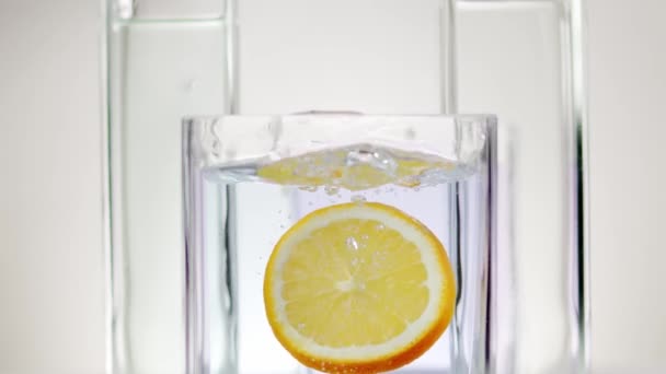 Tranche de citron tombe dans l'eau dans un récipient en verre sur un fond blanc — Video