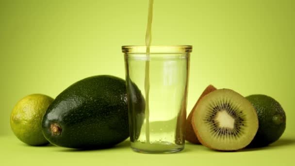 Зеленый фруктовый сок наливая в стакан на минималистском фоне — стоковое видео