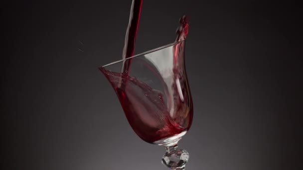 Giet rode wijn in een glanzend glas over een zwarte achtergrond — Stockvideo