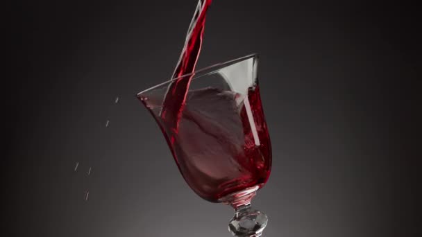 Giet rode wijn in een glanzend glas over een zwarte achtergrond — Stockvideo