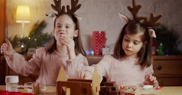Zwei süße Schwestern bauen und dekorieren ein Lebkuchenhaus zu Weihnachten — Stockvideo