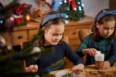 İki tatlı kız kardeş Noel kurabiyesi yapıp süslüyor.