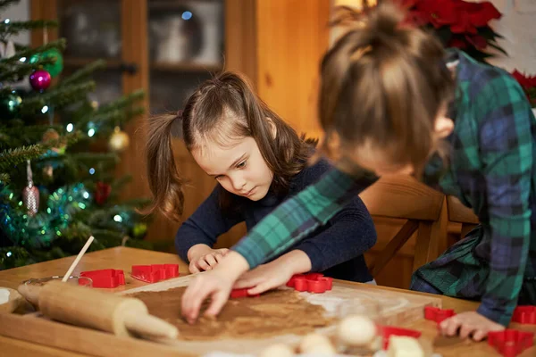 Δύο χαριτωμένες αδελφές κάνουν και διακοσμούν χριστουγεννιάτικα μπισκότα μελόψωμο Royalty Free Φωτογραφίες Αρχείου
