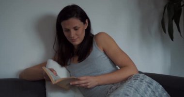 Evdeki genç kadın kanepede oturup oturma odasında kitap okuyor..