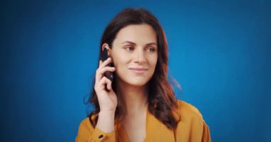 Güzel bir kadın mavi arka planda telefonda konuşuyor.