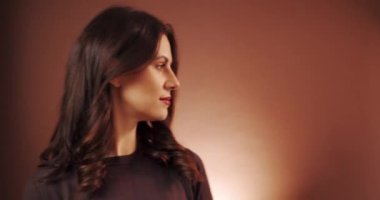 Güzel kadın stüdyoda kahverengi arka planda poz veriyor. 