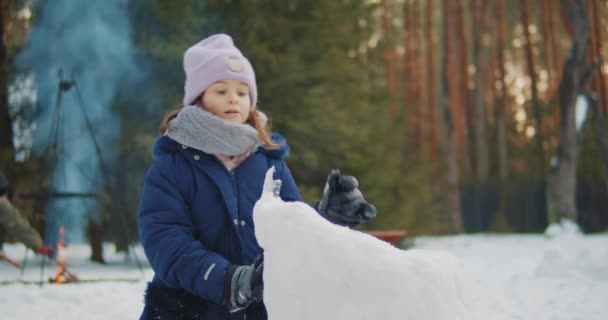 Милая девушка строит и играет в снегу в лесу — стоковое видео