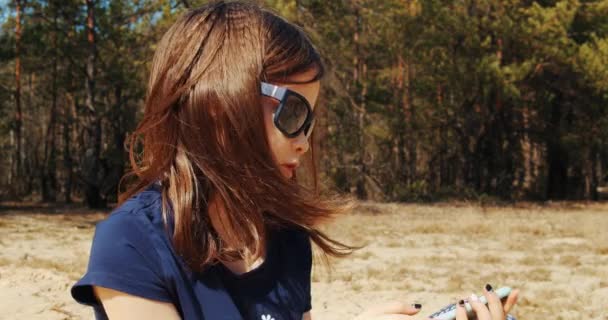 Roztomilá holčička drží telefon v ruce a sedí v letním lese — Stock video