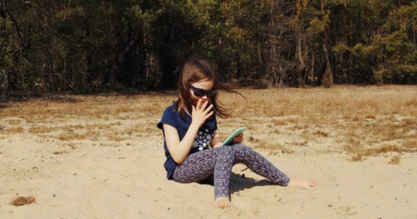 Cute little girl holds phone in hand and sits in summer forest — Stock Video