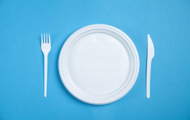 Mavi arka planda beyaz plastik plaka, çatal ve bıçak..