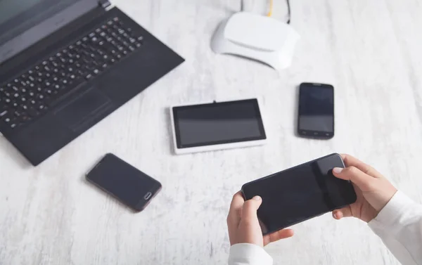 Internet router, laptop, tablet, smartphones on the desk. Hands using smartphone