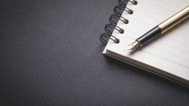 Siyah arkaplan üzerine kalem ve not defteri.