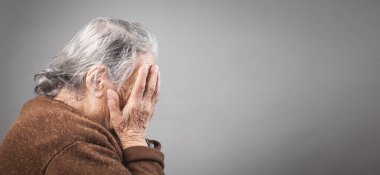 Üzgün yaşlı kadın yüzünü kapatıyor..