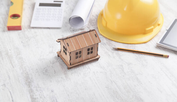 Wooden house model with a helmet, level, document and pencil.