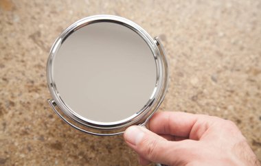 Kahverengi arka planda aynayı tutan bir erkek..