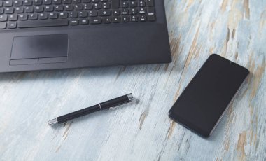 Dizüstü bilgisayar, akıllı telefon ve kalem masanın üstünde..