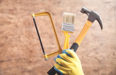 Worker holding hammer, saw, brush.