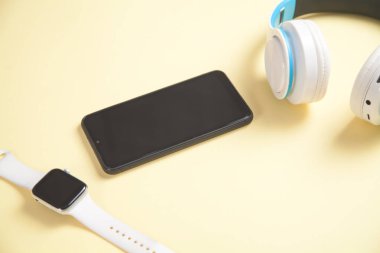Akıllı saat, kulaklık ve sarı arka planda akıllı telefon. Kişisel cihaz. Teknoloji