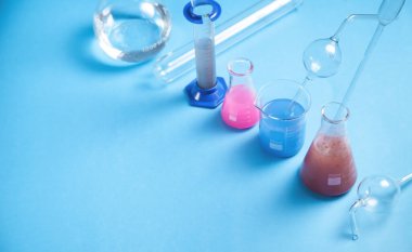 Mavi zemin üzerinde renkli sıvı bulunan bilimsel cam eşyalar.