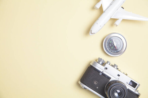 Old camera, toy airplane and compass on yellow background.