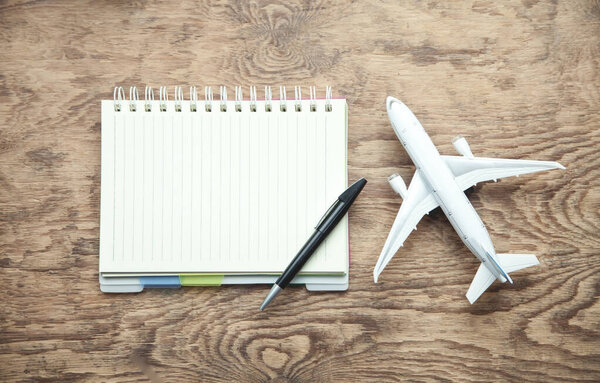 Toy airplane, notepad and pen on wooden background.