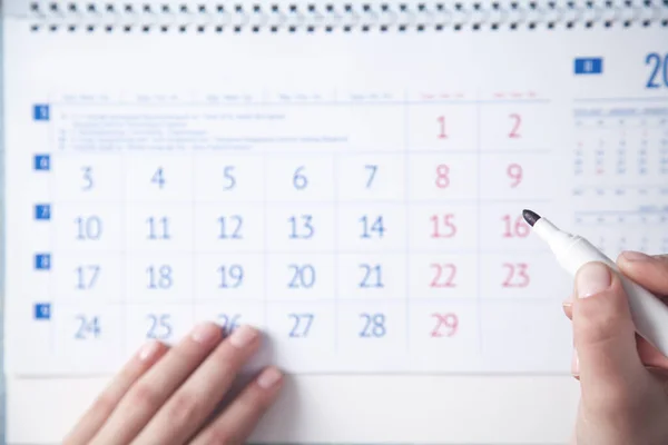 Girl hand marks calendar with a marker.