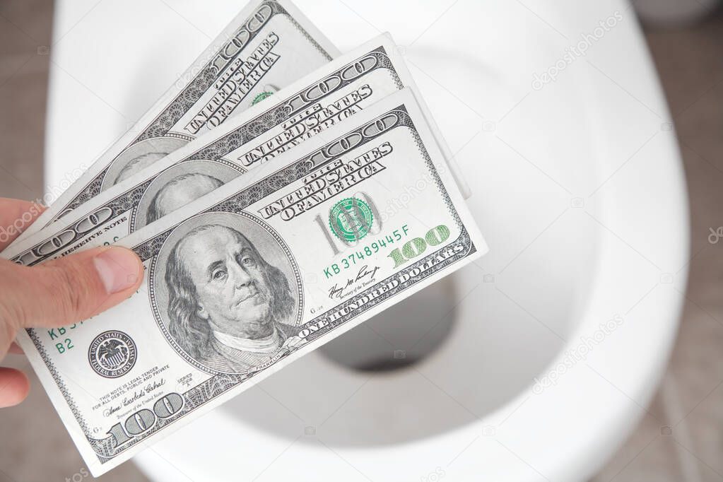 Hand throwing hundred dollars down the toilet.