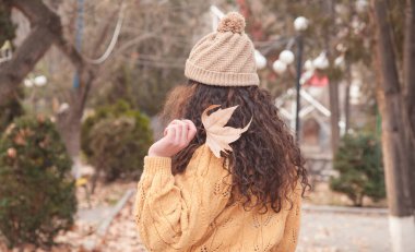 Sonbahar parkında yaprak tutan kadın.