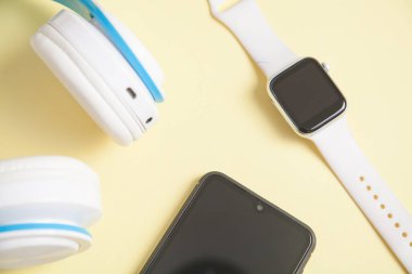 Beyaz kablosuz kulaklık, akıllı telefon ve sarı arka planda akıllı telefon..