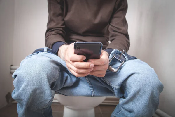 Beyaz adam tuvalette akıllı telefon kullanıyor.