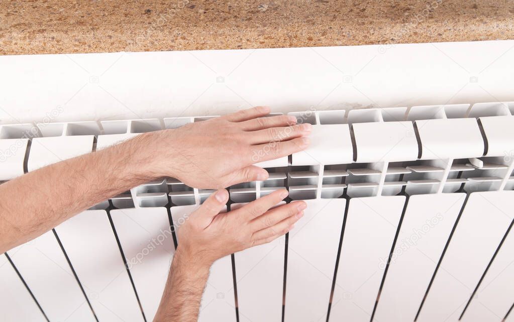 Male hands touch a heating radiator at home.