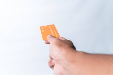 Turuncu renkli kredi kartını temiz beyaz arka planda tutan bir adamın yakın plan fotoğrafı. Ödeme, finans, bankacılık, alışveriş ve çevrimiçi işlemler kavramı. Kopyalama alanı.