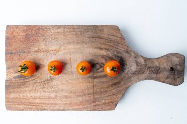 Dört taze kiraz domatesleri, ahşap bir tahtanın üzerinde sıralanmış. Temiz beyaz bir arkaplanda izole edilmiş. Kopyalama alanı olan minimalist gıda kavramı.