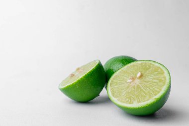 Taze yeşil limonlar, tek parça ve ikiye bölünmüş. Temiz beyaz bir arkaplanda izole edilmiş. Sağlıklı narenciye meyvesi. Soldaki kopyalama alanını çoğalt.