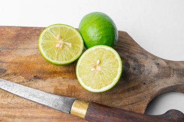 Köy ahşap bir tahtanın üzerinde bıçakla taze yeşil limon (bütün ve dilimlenmiş) yakın plan. Beyaz arkaplan kopyalama alanı sağlar. Yemek pişirme konsepti.