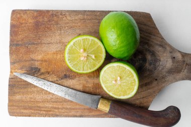 Üst manzara düz yeşil limon yatağı (bütün ve dilimlenmiş) kırsal ahşap bir tahtanın üzerinde bıçakla. Beyaz arkaplan kopyalama alanı sağlar.