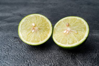 İkiye bölünmüş taze yeşil limonun yakın çekimi. Sulu narenciye meyvesi koyu, dokulu bir arka planda duruyor. Sağlıklı yemek..