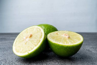 Taze yeşil limon yakın plan, bütün ve dilimlenmiş. Meyve parlak beyaz arka planlı koyu dokulu bir yüzeye dayanır. Boşluğu kopyala.