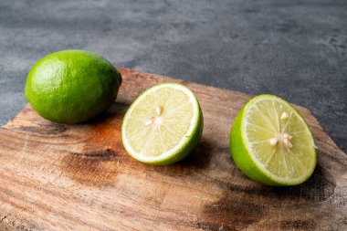 Taze yeşil limon (jeruk nipis) yakın plan, bütün ve dilimlenmiş. Turunçgil meyvesi, koyu renkli ahşap bir kesme tahtasının üzerinde..