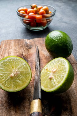 Köy ahşap bir tahtada taze yeşil limon (dilimlenmiş ve bütün) yakın plan. Arka planda bir bıçak ve domates var. Aşçılık / tarif kavramı.