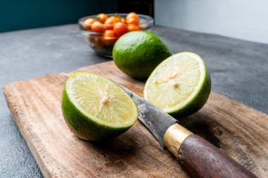 Köy ahşap bir tahtada taze yeşil limon (dilimlenmiş ve bütün) yakın plan. Arka planda bir bıçak ve domates var. Aşçılık / tarif kavramı.