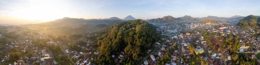 Bajawa, Flores ve Endonezya 'nın geniş hava manzarası. Kasaba tepelerle çevrili sisli bir vadiye yerleşmiştir. Güneş soldan yükseliyor, uzaktaki ikonik Inerie Dağı 'nı aydınlatıyor..