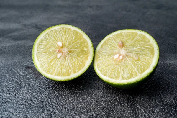 İkiye bölünmüş taze yeşil limonun yakın çekimi. Sulu narenciye meyvesi koyu, dokulu bir arka planda duruyor. Sağlıklı yemek..
