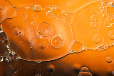 Top view macro photography of bright orange fluid texture featuring scattered bubbles, perfect for abstract artistic backgrounds.