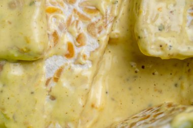Extreme close up of raw fermented soybean cake coated in a savory yellow turmeric batter, ready for frying. Authentic Indonesian food preparation.