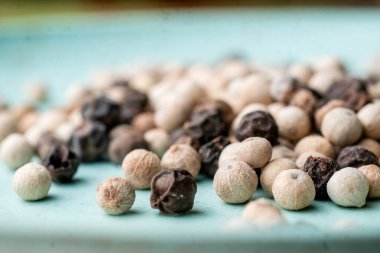 Açık mavi arkaplana saçılmış beyaz ve siyah karabiberlerden oluşan aşırı yakın plan aşçılık için organik baharat dokularını vurguluyor..