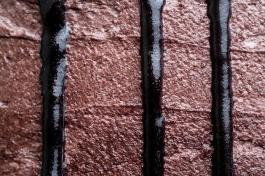Kakaolu pasta üzerine dikey damlayan parlak siyah çikolata ganache 'nin yakın çekim şekli lezzetli bir doğrusal desen oluşturur..