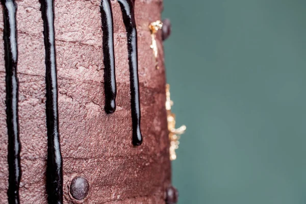 Kakaolu kakaolu kremalı pastadan damlayan koyu çikolata ganache 'nin makro görüntüsü, zarif altın yaprak aksanları ve deniz mavisi arka planı.