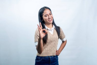 Neşeli Endonezyalı kadın gülümseyerek iyi bir el hareketi gösteriyor. Beyaz bir arka planda memnuniyet, anlaşma ve mükemmelliği temsil ediyor..